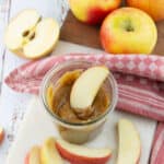 a glass jar with vegan caramel sauce with a sliced apple with more apples in the background