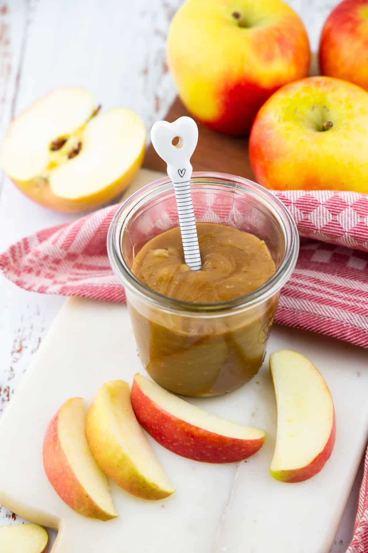 a jar with vegan caramel sauce on a marble chopping board with apples in the background 