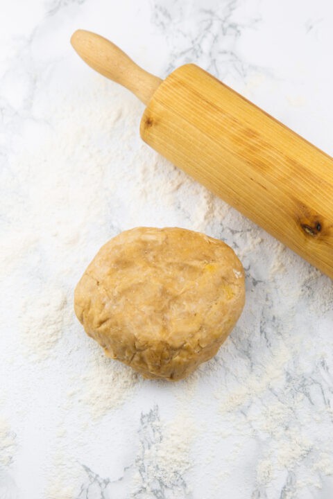 a ball of pie dough on a marble countertop with a rolling pin on the side 