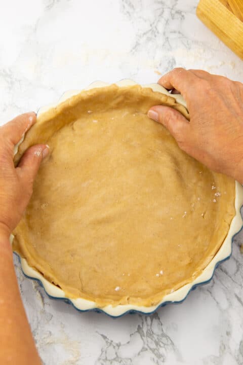 two hands placing vegan pie dough into a pie plate