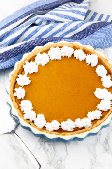 a vegan pumpkin pie decorated with vegan whipped cream on a marble countertop 