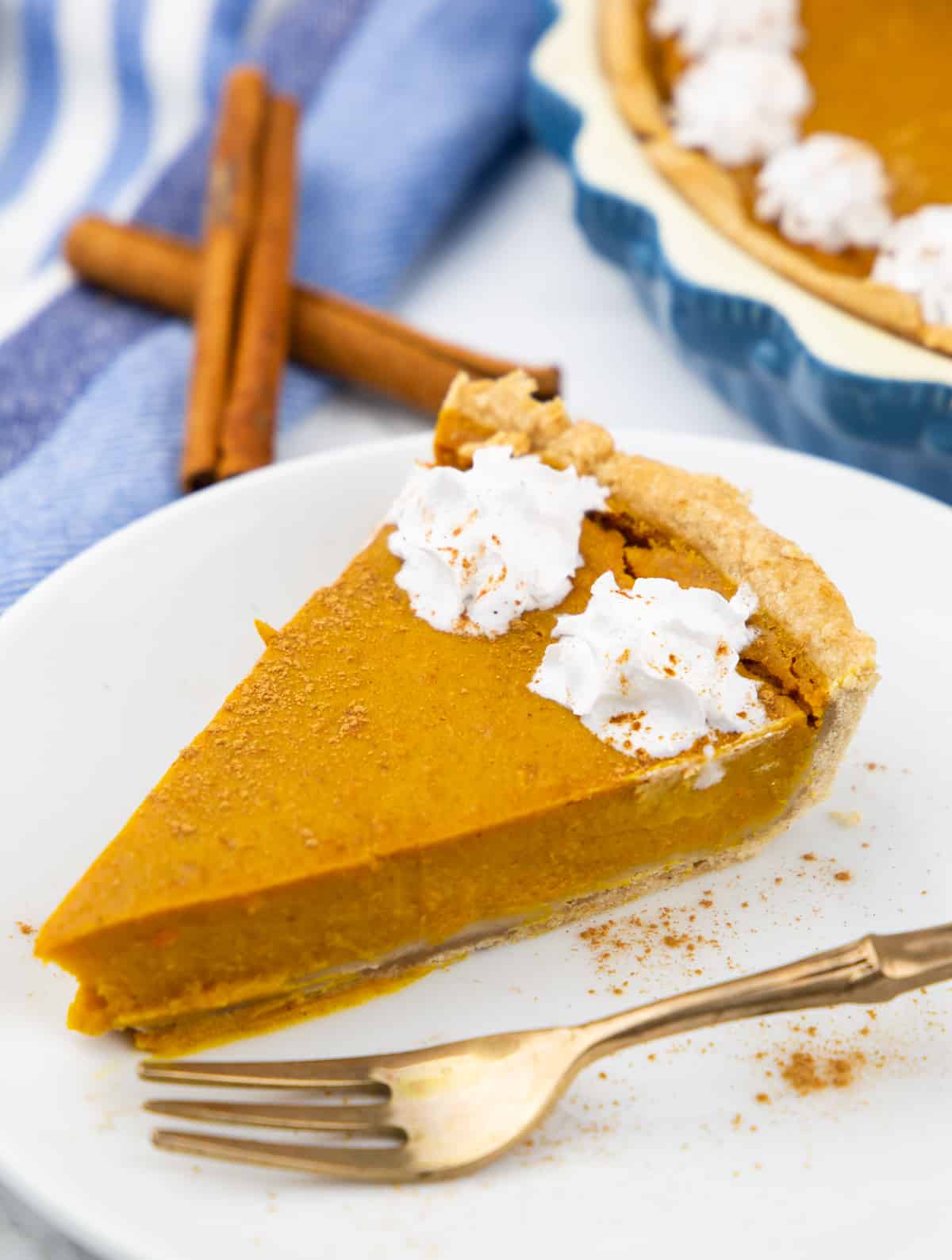 a slice of vegan pumpkin pie on a white plate with a fork on the side and two sticks of cinnamon in the background 