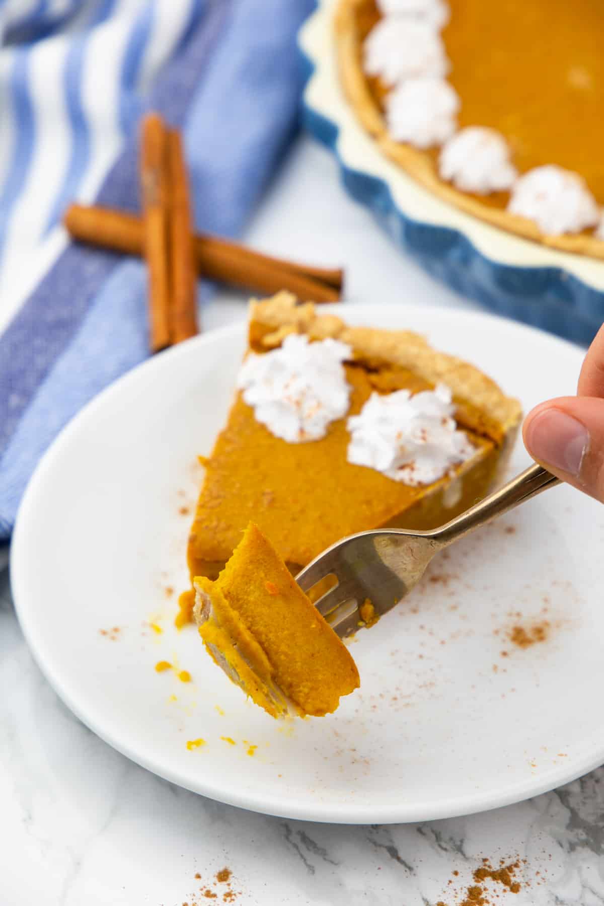 a hand picking up a piece of pumpkin pie with a fork with more pie in the background 