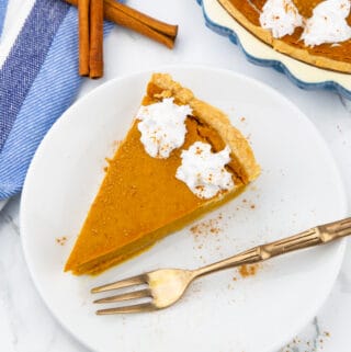 a slice of vegan pumpkin pie on a white plate with a fork on the side
