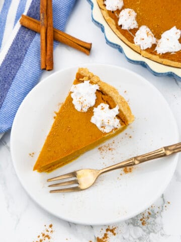 a slice of vegan pumpkin pie on a white plate with a fork on the side