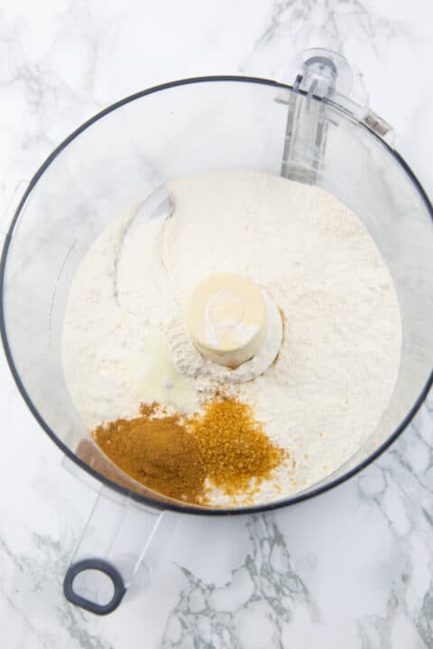 flour, sugar, and cinnamon in a food processor on a marble countertop 