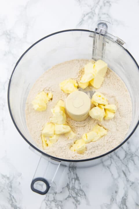 flour and vegan butter in a food processor on a marble countertop 