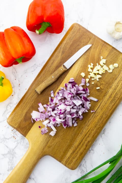 finely chopped red onion and garlic on a wooden chopping board with a knife on the side