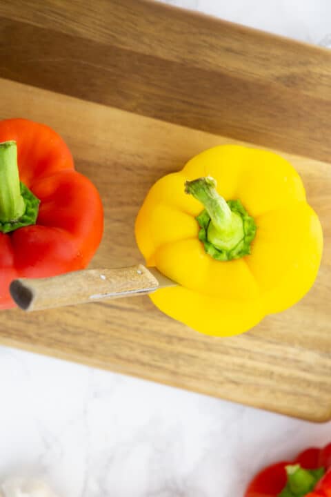 two bell peppers with their top cut off on a wooden chopping board