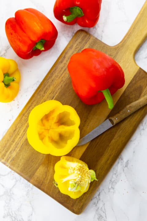 a yellow bell pepper with core and seeds pulled out on a wooden chopping board with a knife on the side