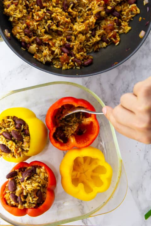 a hand filling four stuffed peppers in a glass casserole dish
