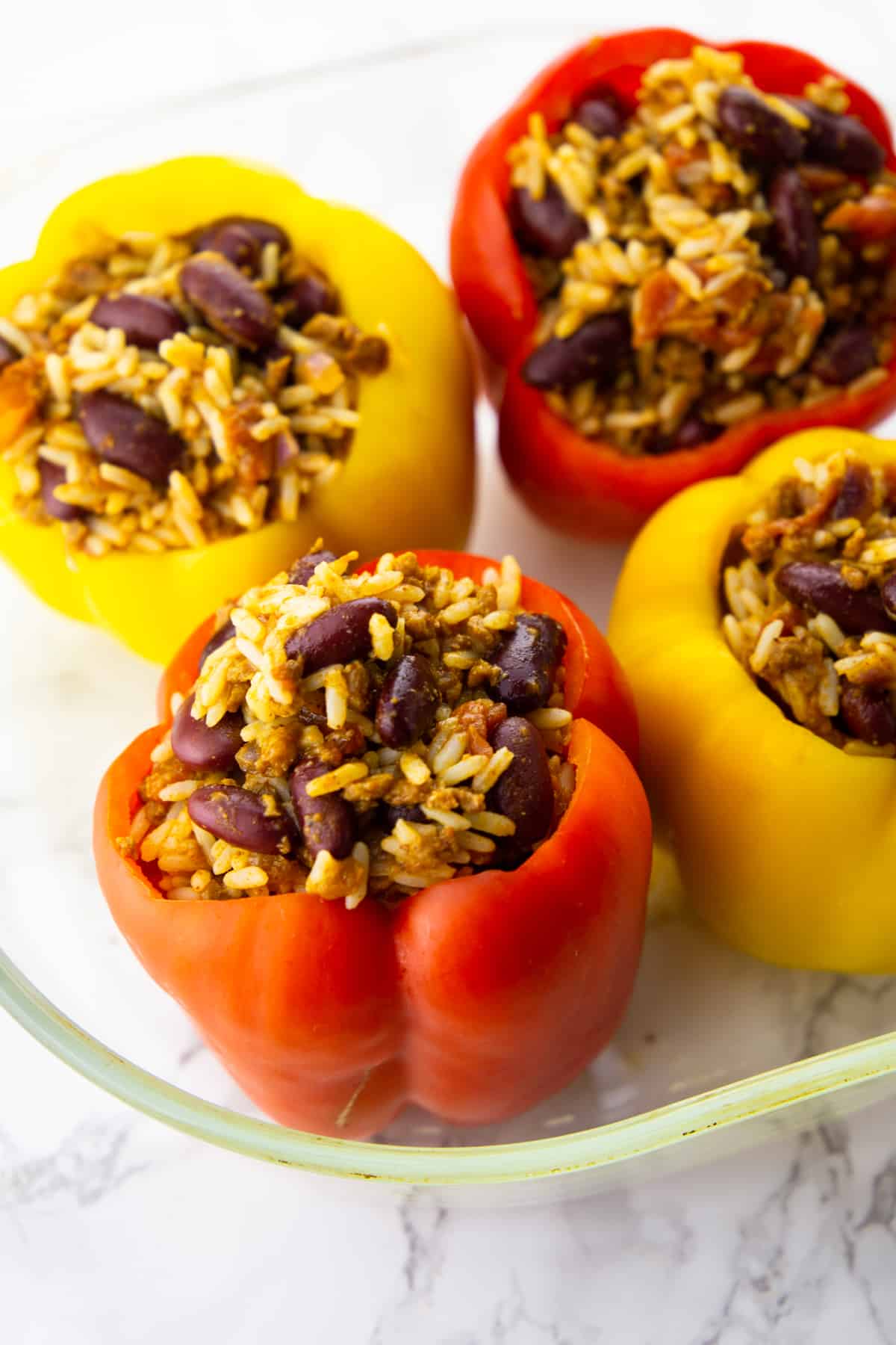 four vegan stuffed peppers in a glass casserole dish on a marble countertop 