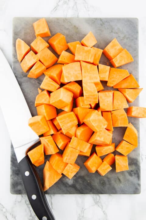 cubed sweet potato on a marble chopping board with a large knife on the side 