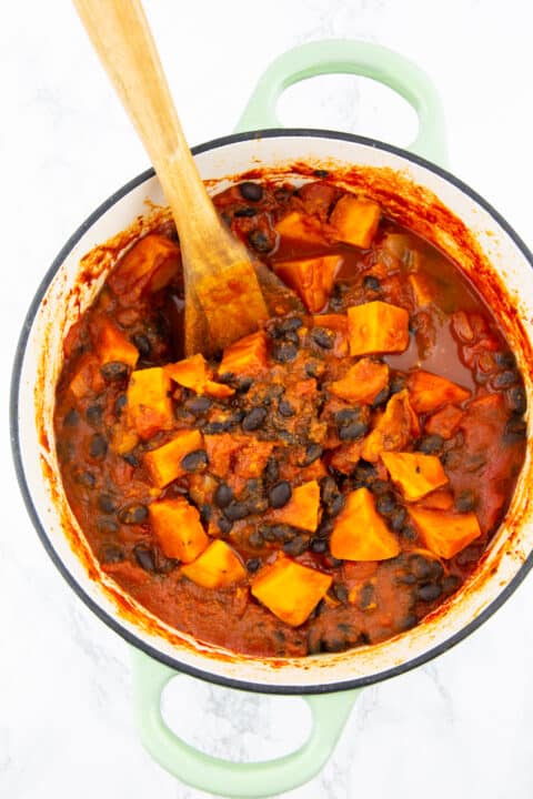 a green pot with sweet potato and black bean chili on a marble countertop 