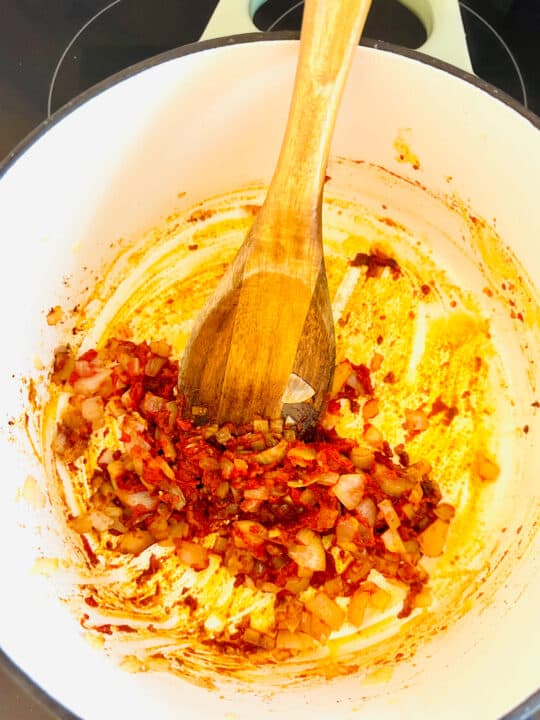 a white pot with sautéd onion, tomato paste, and spices with a wooden spoon 