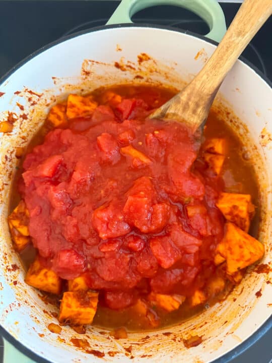 sweet potatoes in a white pot with canned tomatoes and a wooden spoon 