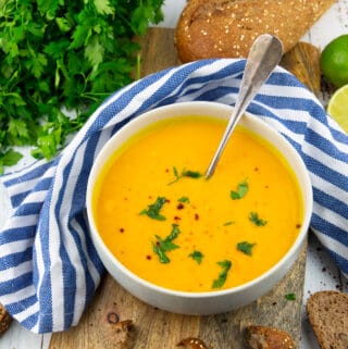 a grey bowl with sweet potato soup sprinkled with chopped parsley on a wooden board with a loaf of bread in the background