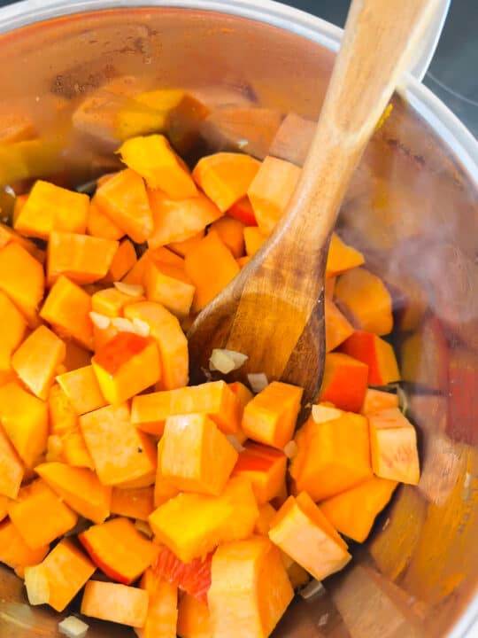 sweet potato and squash cubes in a pot with a wooden spoon 