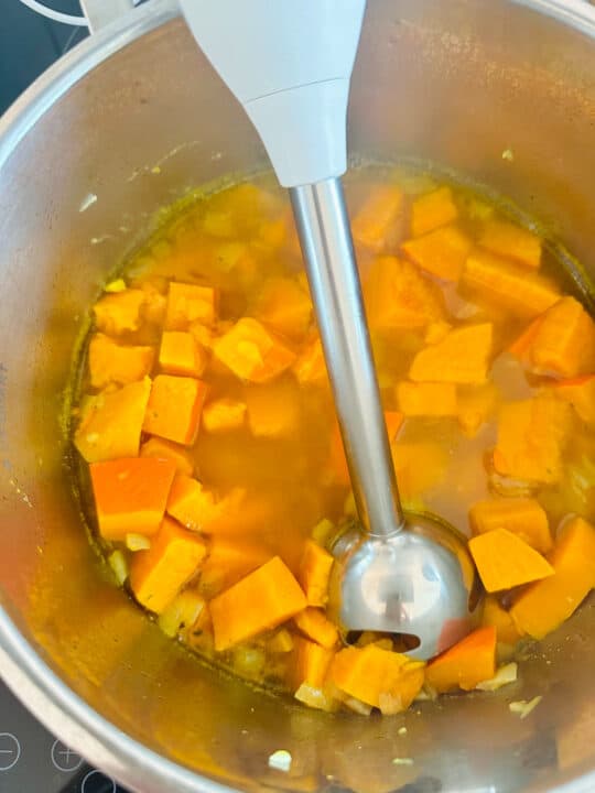 cubed sweet potatoes and squash in a pot with an immersion blender 