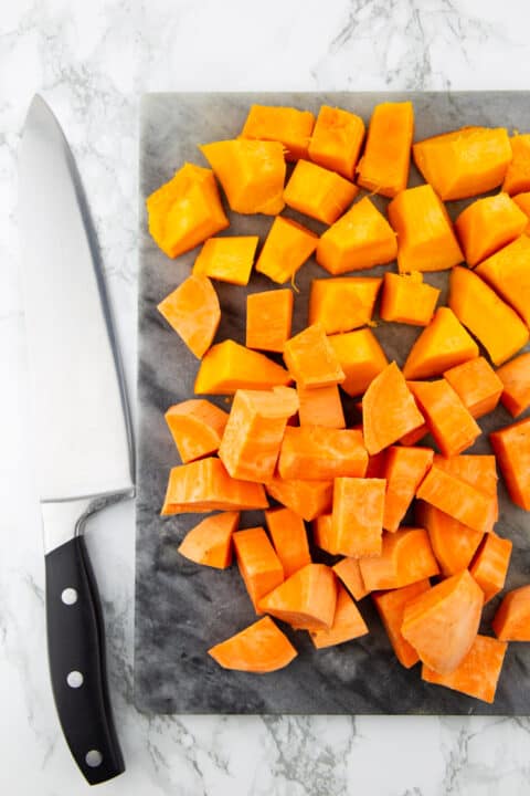 sweet potato cubes on a marble chopping board with a large knife on the side 