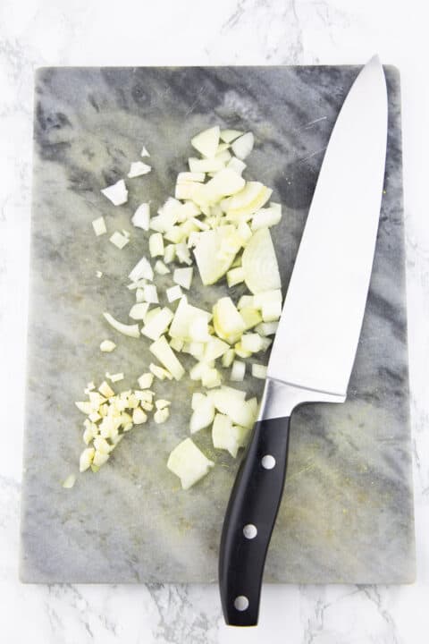 finely chopped onion on a marble chopping board with a large knife on the side 