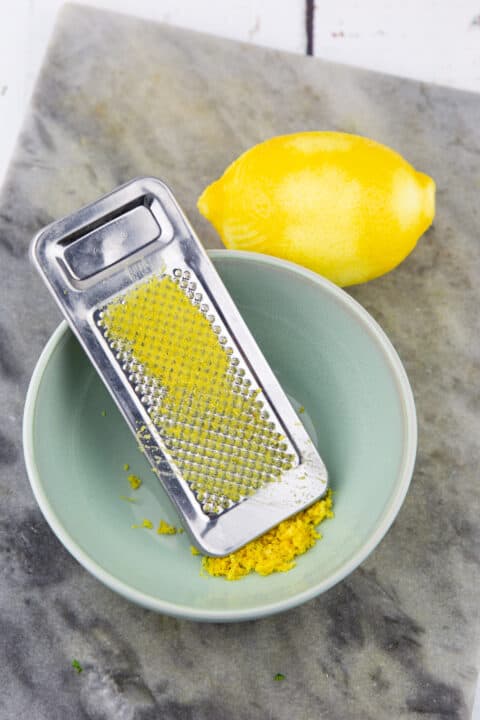 a lemon on a marble chopping board with a small bowl and a grater 
