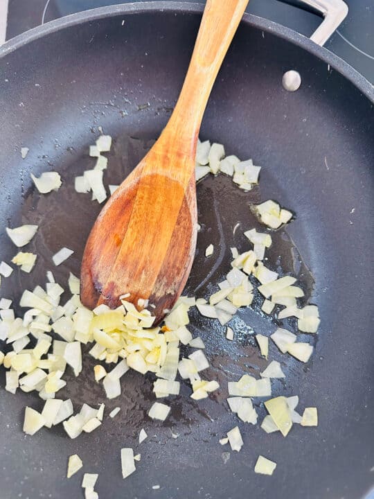 sautéd onion and garlic in a black pan with a wooden spoon 