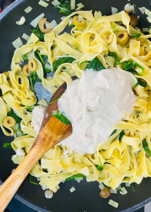 fettuccine in a black pan with olives, baby spinach, and tahini sauce 