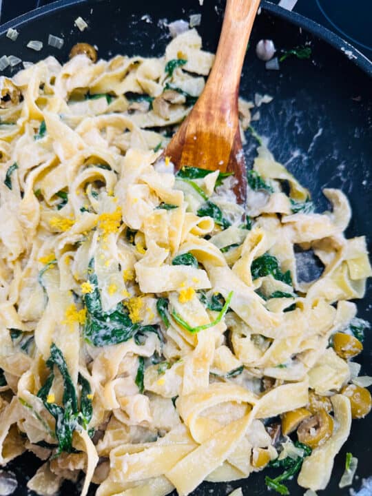 a black pan with lemon tahini pasta with a wooden spoon 