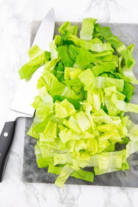 chopped Romain lettuce on a marble chopping board with a large knife on the side 