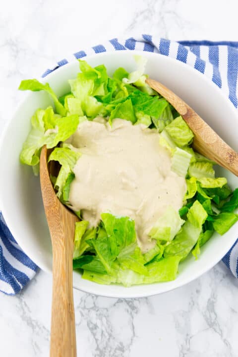 a white bowl with chopped lettuce and vegan Ceasar salad dressing with wooden salad cutlery 