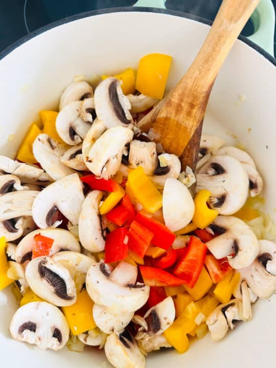 bell pepper and mushrooms in a white pot with a wooden spoon 
