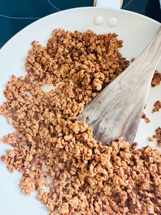 vegan ground beef crumbles in a white pan with a wooden spoon 