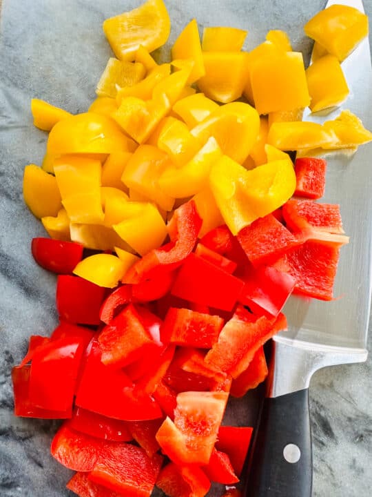 diced yellow and red bell pepper on a marble chopping board with a knife on the side 