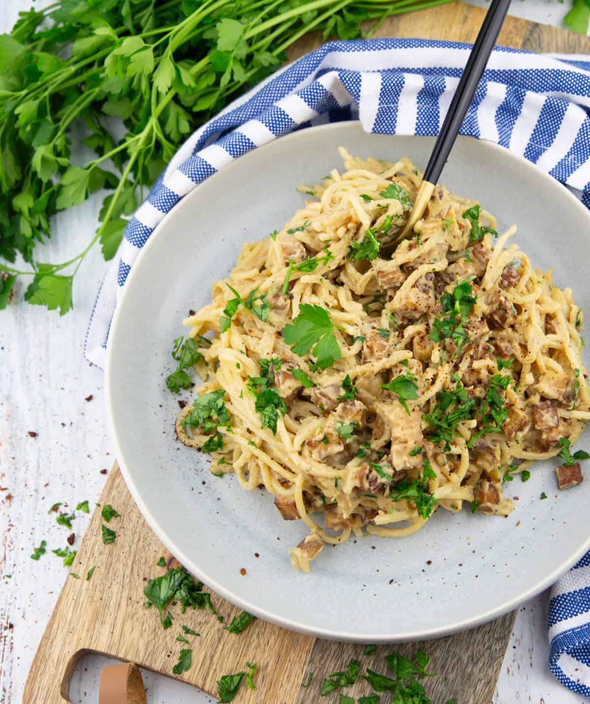 vegan carbonara in a grey plate on a wooden board with a bunch of parsley in the background 