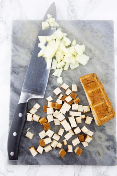 cubed smoked tofu and finely chopped onion on a marble chopping board with a large knife