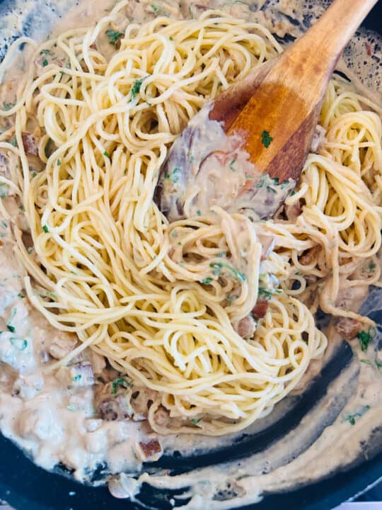 a black pan with cooked spaghetti and a cashew sauce with a wooden spoon 
