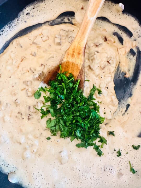 vegan carbonara sauce in a black pan with finely chopped parsley and a wooden spoon 