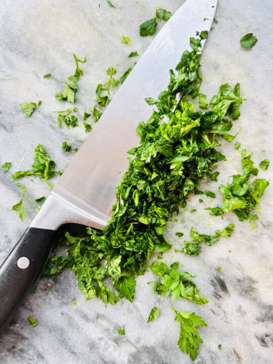finely chopped parsley on a marble chopping board with a large knife 