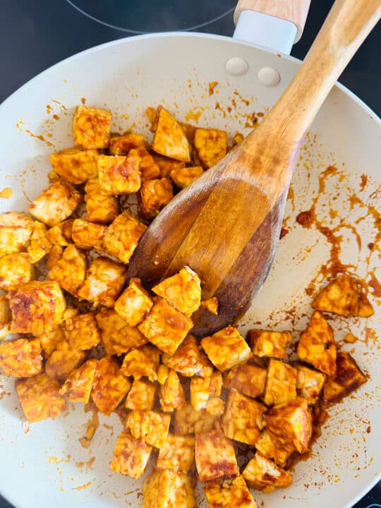 pan-fried tempeh cubes in a white pan with a wooden spoon 