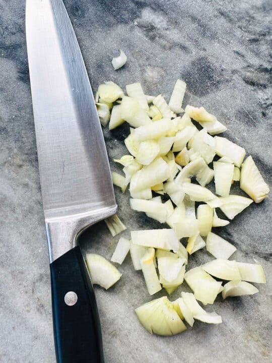 finely chopped onion on a marble chopping board with a large knife 