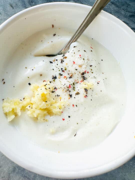 a white bowl with vegan yogurt, minced garlic, salt, and pepper, and a spoon 