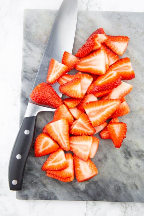 chopped strawberries on a marble countertop with a large knife on the side