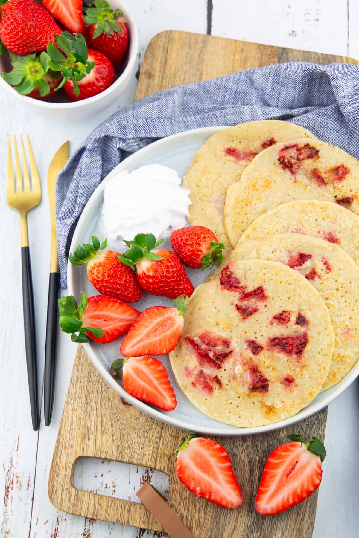 a grey plate with five vegan strawberry pancakes on a wooden board with cutlery on the side 