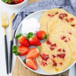 five strawberry pancakes on a grey plate with whipped cream and halved strawberries on the side