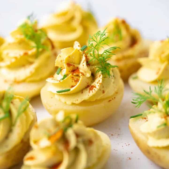vegan deviled eggs on a white plate sprinkled with paprika and fresh dill