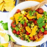 a white bowl with corn avocado tomato salad on a wooden board with limes on the side