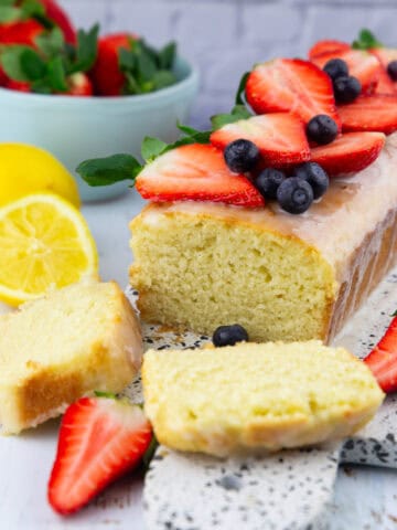 a lemon olive oil cake on a marble board with a bowl of strawberries in the background