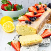 a lemon olive oil cake on a marble board with a bowl of strawberries in the background