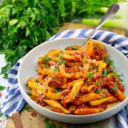 a grey plate with sausage fennel pasta on a wooden board with with parsley and fennel in the background